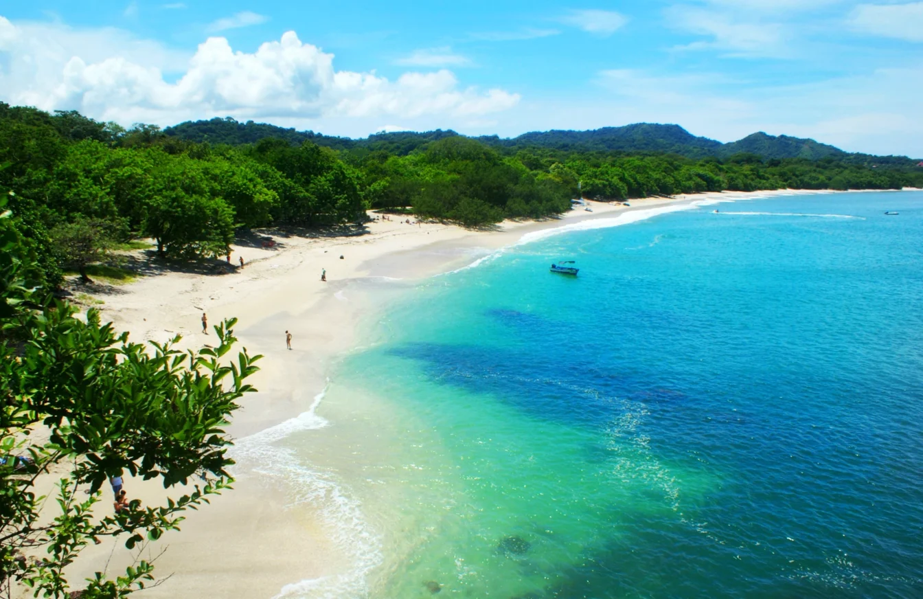 Imagen de Playa Carrillo en Costa Rica en la que aparece una frondosa vegetación, arena blanca y agua en tonos azul intenso y turquesas