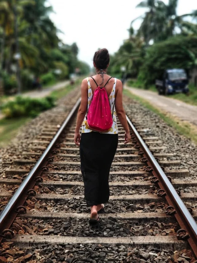 Imagen de una mujer de espaldas mientras camina por el centro de las vías de un ferrocarril
