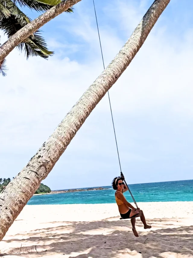 Imagen de una mujer sonriente subida a un columpio sujeto a una palmera mientras disfruta en la playa