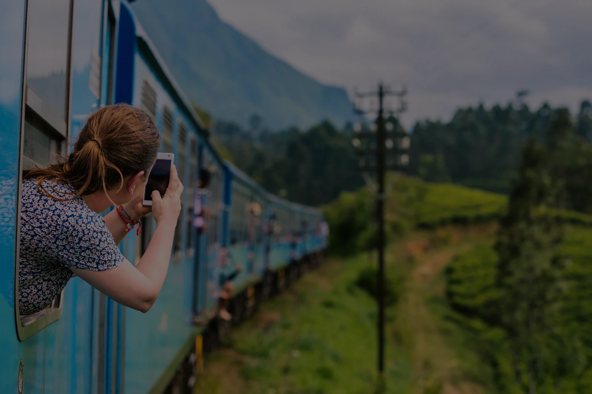 Imagen panorámica de un tren realizando una curva abierta hacia la derecha mientras una mujer saca su cuerpo por una venta para realizar un fotografía con su móvil