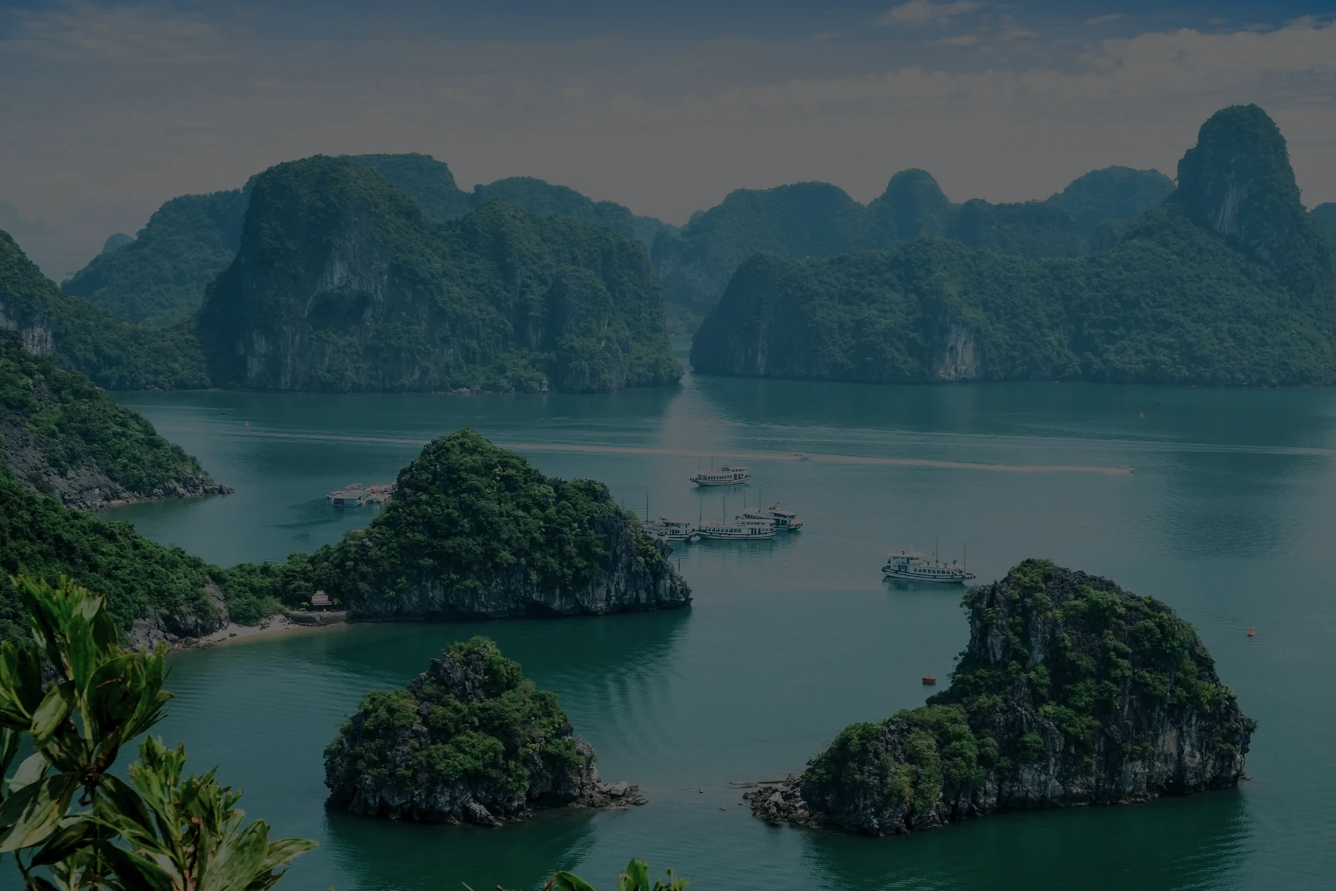 Imagen de un archipiélago de pequeñas islas e islotes de Vietnam con frondosa vegetación, aguas turquesas y varios barcos fondeados